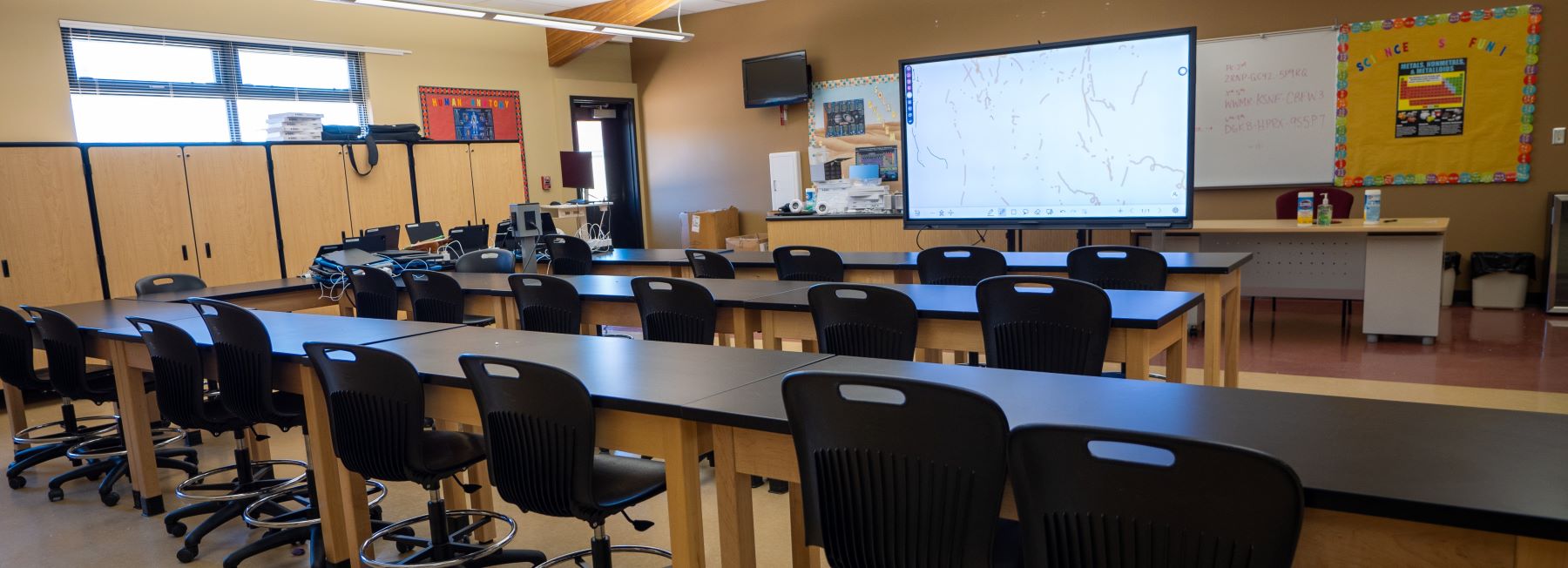 A classroom with desks and chairs arranged in front of a projector screen for educational purposes.