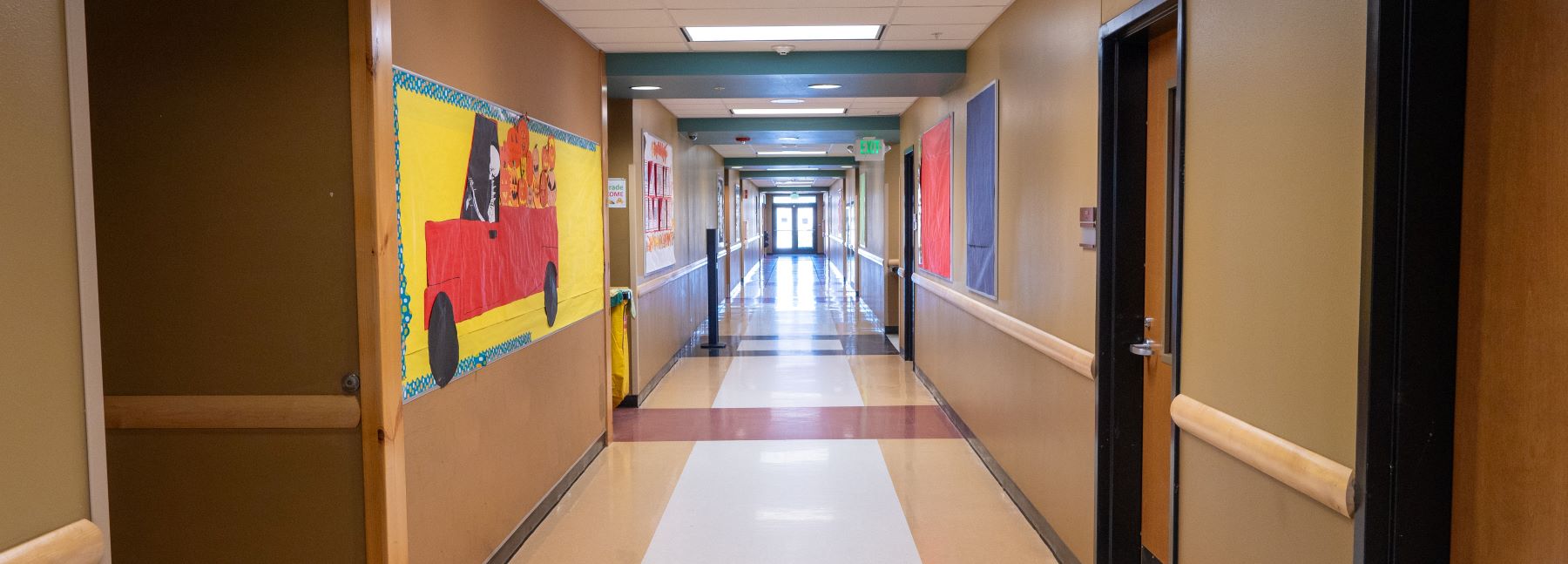 looking down hallway with classroom doors on each side and exterior doors with light shining through at end