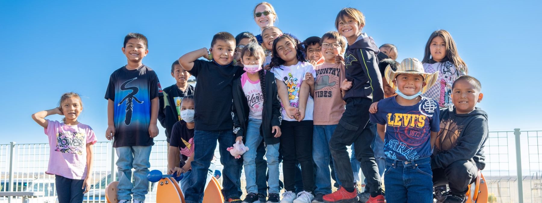 Teacher and group of students in playground on a sunny day.